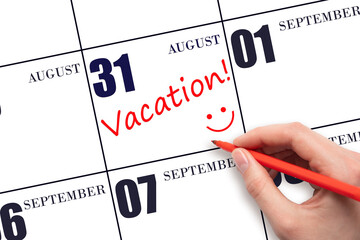 A hand writing a VACATION text and drawing a smiling face on a calendar date 31 August. Vacation planning concept.