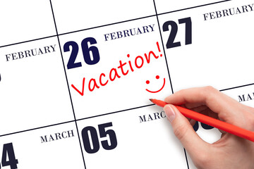 A hand writing a VACATION text and drawing a smiling face on a calendar date 26 February. Vacation...