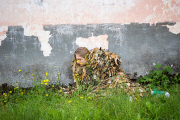 a young girl lies in the grass in a camouflage military costume near the old wall of an abandoned building