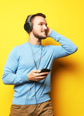 Naklejka premium Portrait of a young man wearing blue sweater and headphones listening to music and enjoying life over yellow background