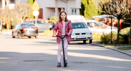 Fototapeta na wymiar Funny little girl rides a kick scooter