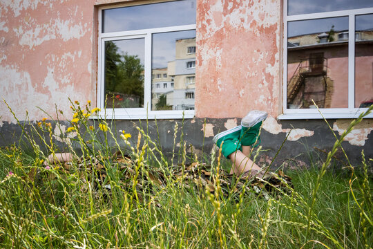 a young girl lies in the grass in a camouflage military costume near the old wall of an abandoned building