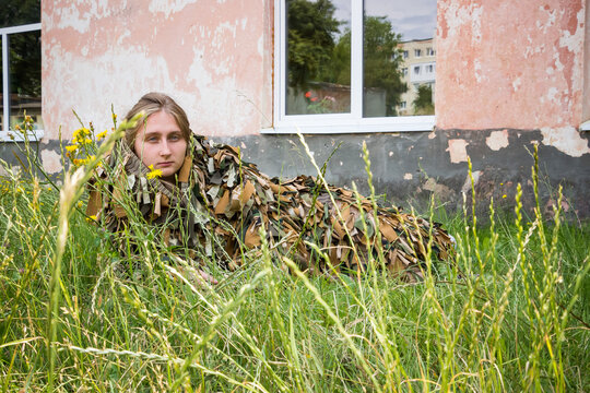 a young girl lies in the grass in a camouflage military costume near the old wall of an abandoned building