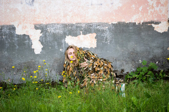a young girl lies in the grass in a camouflage military costume near the old wall of an abandoned building