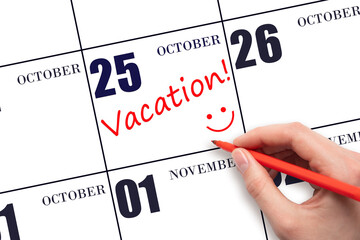 A hand writing a VACATION text and drawing a smiling face on a calendar date 25 October. Vacation...