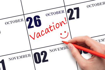 A hand writing a VACATION text and drawing a smiling face on a calendar date 26 October. Vacation...