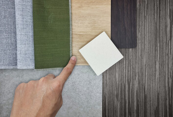 architect's hand selecting interior material samples in board consisting white artificial stone, grey and green curtain fabrics, oak wooden and concrete vinyl floorings, Italian walnut veneers.