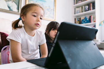 Two little girls attentively watching a video on a tablet in their living room. Concept of childhood, technology, learning, having fun, the Internet and connectivity.