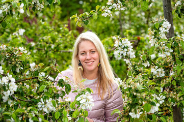 closeup portrait of a smiling blonde woman in a blossoming garden in spring, selective focus