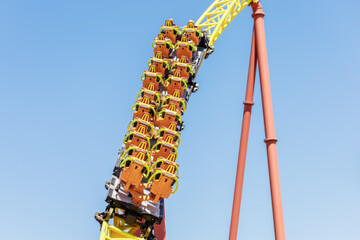 A trolley with orange seats speeds up a yellow rollercoaster against a blue sky. Extreme attraction in the amusement park. Closeup photo. Defocused image © jockermax3d