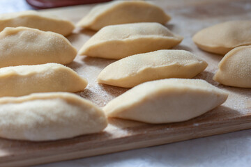 Fototapeta na wymiar Aesthetic semi-finished products. Raw dumplings on a wooden board. Fast food