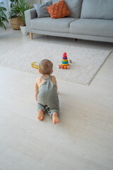 Vertical shot of cute funny infant crawling along floor, looking at his eco friendly wooden...