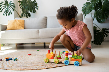 Black lovely toddler in pink t shirt playing with a wooden train. Little girl play with wooden...