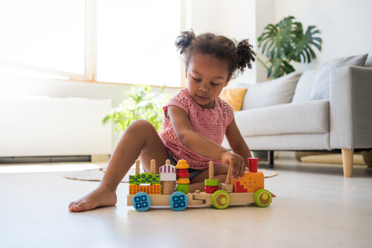 Concentrated black child girl playing with colourful wooden train at the floor. Toddler having fun and building out of bright constructor bricks. Developing toys concept