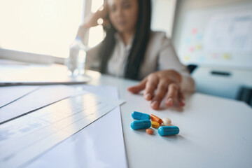 Company employee seated in workplace choosing headache medicine
