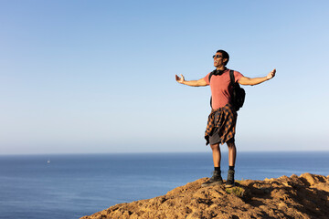 Young man standing on the stone with raised up arms. Tourist man on the top of the mountain..
