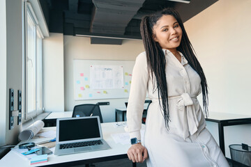 Joyous modern businesswoman posing for camera in her workplace