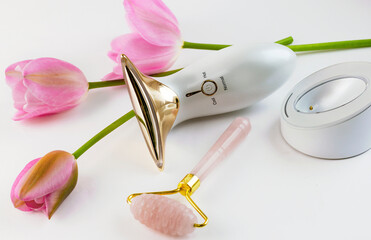 Obraz na płótnie Canvas microcurrent massager and quartz roller on a white background with pink tulips. High quality photo