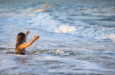 Girl with wet hair in a leopard swimsuit splashes water while sitting in the sea