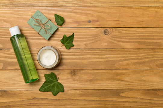 Cosmetic products with ivy extract on wooden background, top view