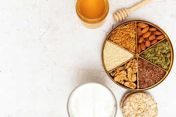 A round plate with nuts and seeds, honey, bread and milk stand on a table with a light background. Concept: proper nutrition, breakfast, healthy food.