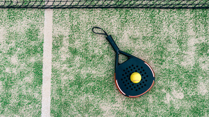 Yellow ball on top of the padel racket and behind net on green court grass turf