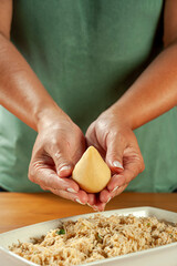 Woman hands holding brazilian croquette (coxinha de frango) on a wooden kitchen table