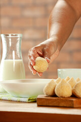 Woman hands breading brazilian croquette (coxinha de frango) with breadcrumbs on a wooden kitchen table.