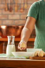 Woman hands breading brazilian croquette (coxinha de frango) with breadcrumbs on a wooden kitchen table.