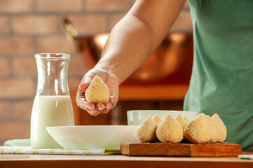 Woman hands breading brazilian croquette (coxinha de frango) with breadcrumbs on a wooden kitchen table.