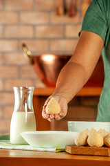 Woman hands breading brazilian croquette (coxinha de frango) with breadcrumbs on a wooden kitchen table.
