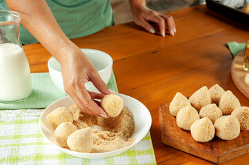 Woman hands breading brazilian croquette (coxinha de frango) with breadcrumbs on a wooden kitchen table.
