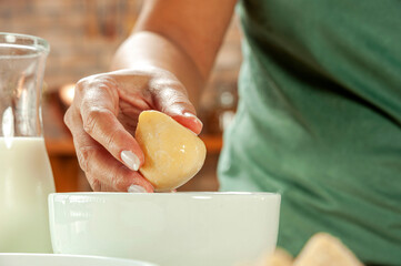Woman hands breading brazilian croquette (coxinha de frango) with breadcrumbs on a wooden kitchen table.