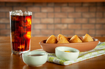 Fried brazilian croquettes (coxinha de frango) with iced soda in a kitchen with bricks wall.