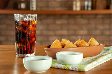 Fried brazilian croquettes (coxinha de frango) with iced soda in a kitchen with bricks wall.