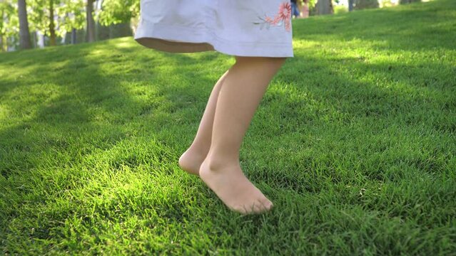 Close-up of a little girl in a dress jumping on a beautiful lawn with bare feet at sunset.Happy childhood in the fresh air,bright emotions.A child jumps on the grass. A child is having fun in the park