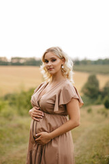 A pregnant woman in a dress touches her belly in a wheat field at sunset. The pregnancy concept. 