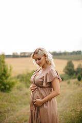 A pregnant woman in a dress touches her belly in a wheat field at sunset. The pregnancy concept. 
