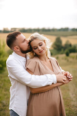 Fototapeta premium Loving man hugging his pregnant wife from behind in nature.