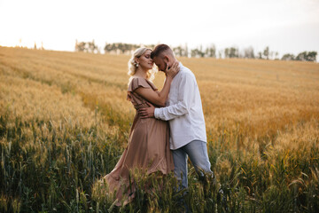 Man and his pregnant wife are hugging in wheat field at sunset.