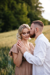 A man is holding hands of pregnant wife in a field at sunset.