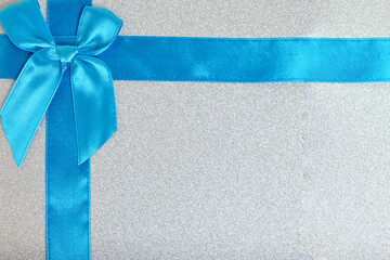 Blue ribbon tied with bow on a shiny gift box.