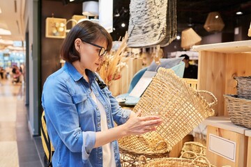 Mature woman shopper choosing interior wicker baskets in home decor store
