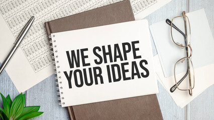 we shape your ideas text on notepad with glasses, pen and charts