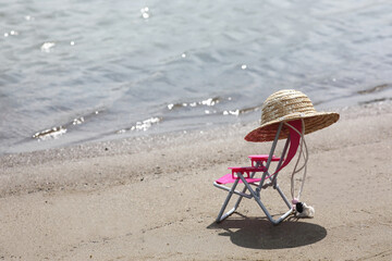 straw hat on the back of chaise longue on a beach near waterline