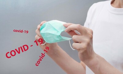 A woman in a white T-shirt holds a medical mask in which the inscriptions 