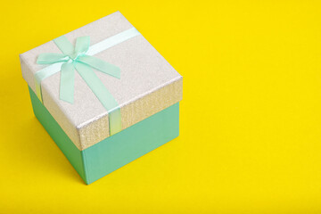 Turquoise gift box is tied with ribbon with bow on yellow background.