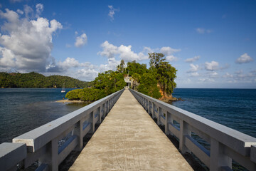 Fototapeta premium bridge over the sea to a small green tropical island, blue sky with clouds