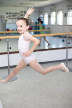 Cute little girl toddler ballerina in pale pink tutu and ballet shoes practicing dance jump.