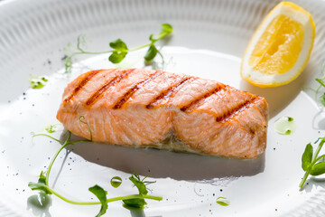 Salmon steak on the grill with greenery and lemon on a white plate with reflection macro close up